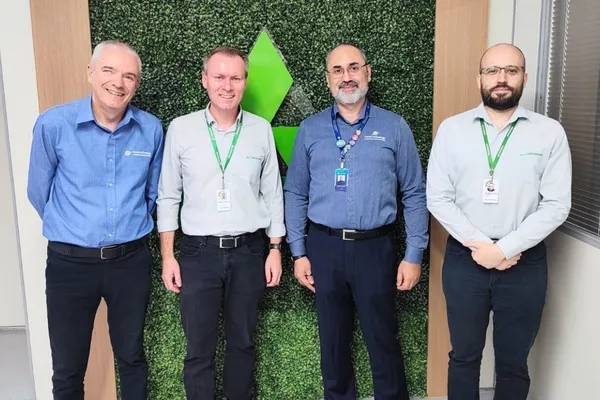 Quatro homens posam para a foto em frente a um painel verde com o logotipo da Cotrirosa. Eles vestem camisas sociais com identificação da empresa e crachás. Dois deles usam camisas azul-escuras com logos do Sistema Ocergs, enquanto os outros dois vestem camisas cinza com logos da Cotrirosa. Todos sorriem ou mantêm uma postura formal, representando a parceria entre as entidades.