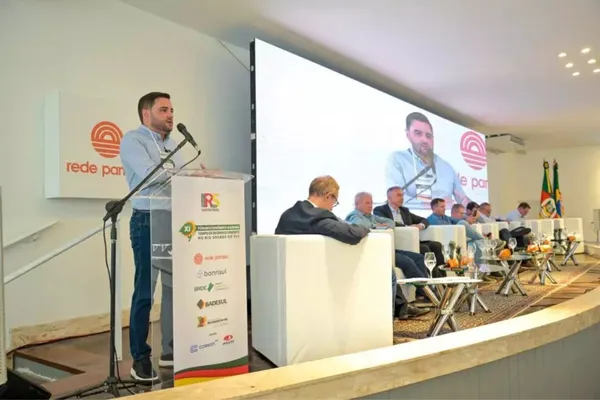 O XI Fórum Econômico Gaúcho – Tempo de Desenvolvimento reuniu importantes lideranças dos setores público e privado para debater estratégias para o crescimento do Rio Grande do Sul. A imagem mostra um dos palestrantes discursando no evento, que foi promovido pela Rede Pampa e contou com a presença de autoridades e representantes de diversas instituições. Ao fundo, um grande telão exibe a transmissão ao vivo, enquanto participantes acompanham a programação no palco.