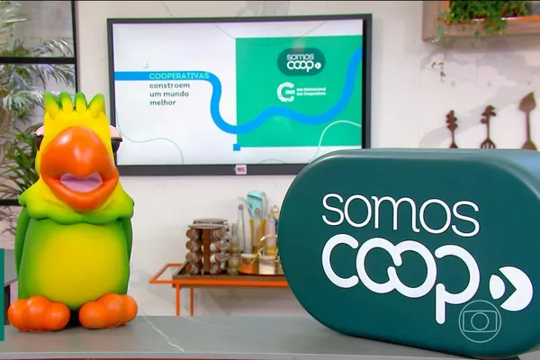 Imagem do papagaio Louro José ao lado do logo “Somos Coop”, com tela ao fundo exibindo a frase “Cooperativas constroem um mundo melhor”, durante programa da TV Globo.
