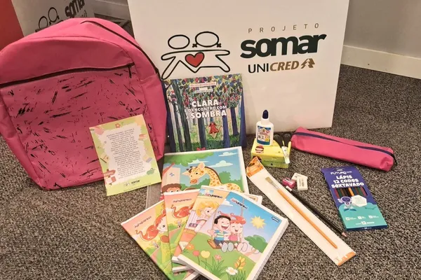Kit escolar do Projeto Casulo inclui mochila rosa, estojo, livros infantis, cadernos, lápis de cor, régua, cola e outros itens de papelaria, com caixa do Projeto Somar ao fundo.