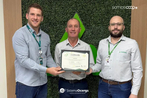 Representantes da Cotrirosa exibem o Certificado de Energia 100% Renovável, concedido pela Ludfor Energia, em frente a painel com símbolo verde da cooperativa. 