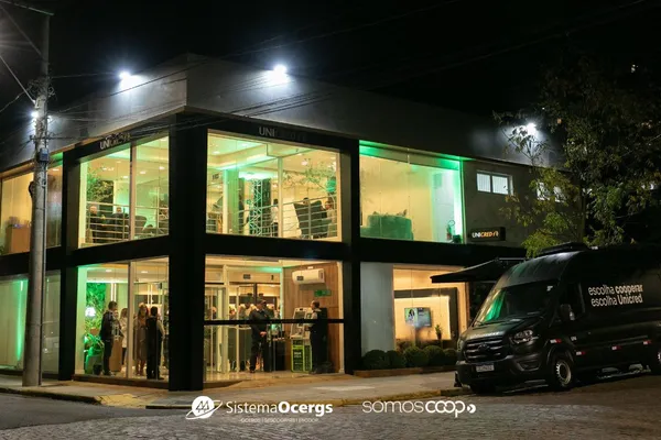 Fachada noturna da agência revitalizada da Unicred Ponto Capital em Cachoeira do Sul, com iluminação verde e ambientes internos visíveis, destacando modernidade e acolhimento.