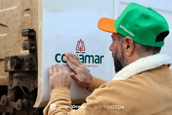 Cooperado aplica adesivo com a nova logomarca da Cotramar em caminhão, simbolizando o início de uma nova fase visual e institucional da cooperativa de transporte de Marau.