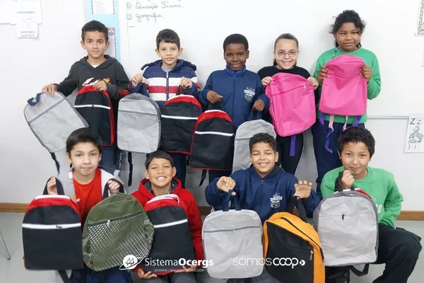 Alunos da Escola Estadual Fernandes Vieira, em Lajeado, posam sorridentes em sala de aula segurando mochilas coloridas doadas pela Unicred Premium em ação de educação financeira.