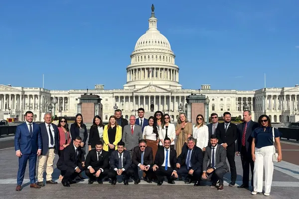 ssa imagem mostra um estande do Sistema Ocergs em um ambiente praiano. O estande tem uma temática de verão, com decoração que remete à praia, incluindo boias, pranchas, conchas e cadeiras de descanso. Há uma placa colorida com setas apontando para diferentes direções e palavras como "Cooperativismo", "Verão", "Churrasco" e "Sol". Pessoas interagem dentro e ao redor do espaço, que conta com mesas altas e decoração tropical, como plantas e abacaxis. Ao fundo, há um banner com a frase "Se tem verão, tem cooperativismo" e imagens de uma praia movimentada.