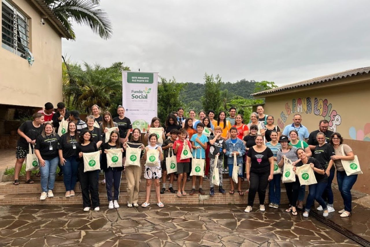 Grupo de alunos e educadores posa com ecobags em frente à Escola Ana Lobler, em Nova Palma/RS, durante atividade do projeto Multiplicadores Lixo Zero apoiado pelo Fundo Social do Sescoop/RS.