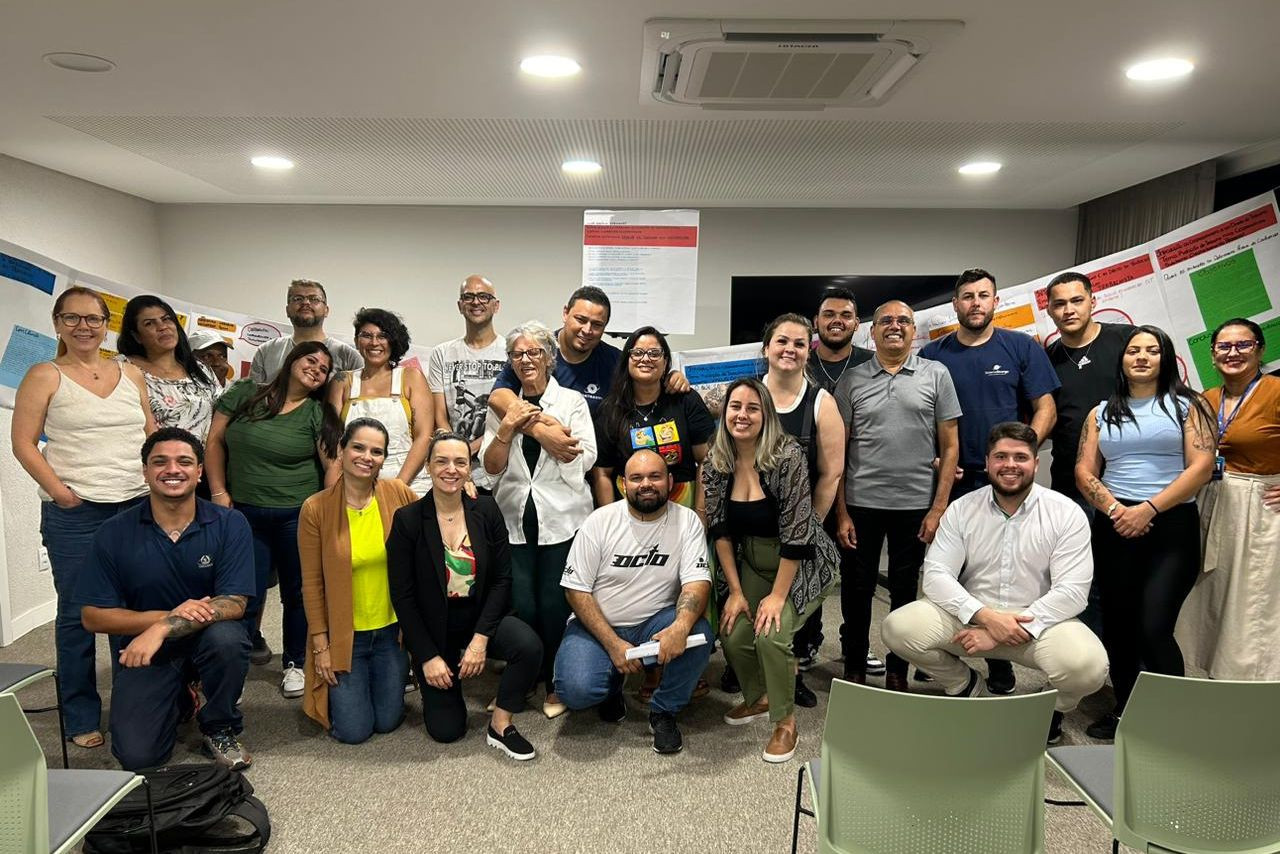 Semana Acadêmica 2024 | Crédito: Sistema Ocergs Participantes do grupo posam sorridentes em atividade da Escoop, com cartazes coloridos ao fundo, durante encontro de pesquisa e cooperação.