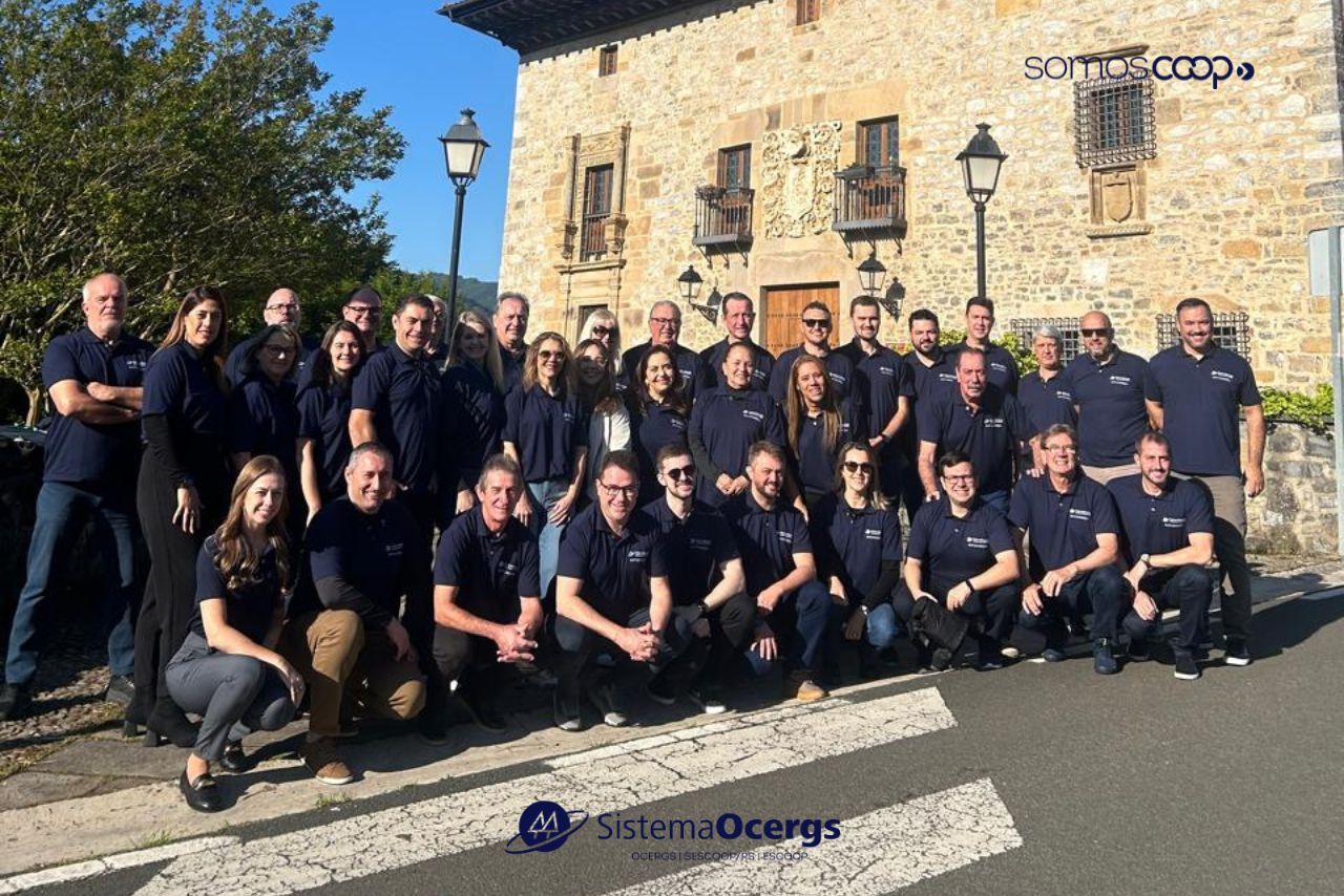 Grupo de cooperativistas gaúchos participantes da missão técnica do Sistema Ocergs à Mondragon, na Espanha, reunidos em frente a um prédio histórico no País Basco, todos vestindo camisetas oficiais.