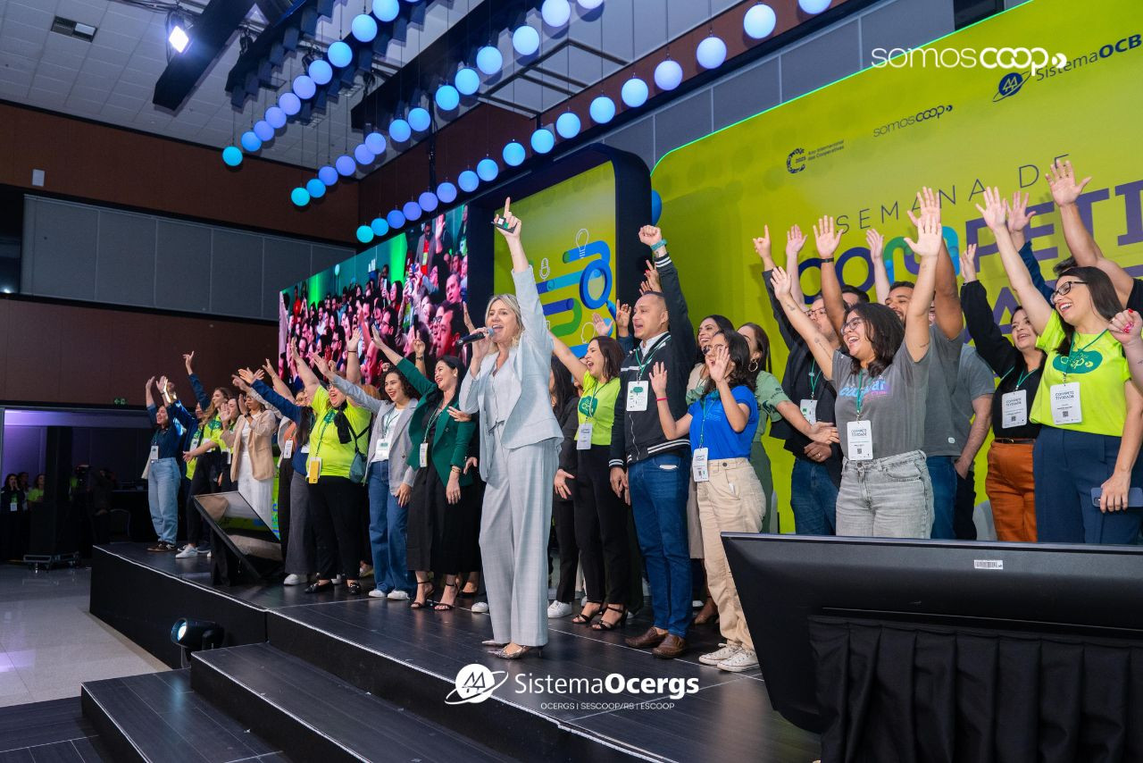 Comunicadores de cooperativas celebram no palco durante o encerramento da Semana da Competitividade 2025, em evento promovido pelo Sistema OCB, com clima de união e entusiasmo coletivo.