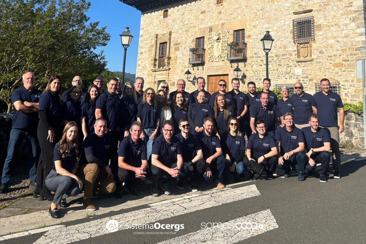 Grupo de cooperativistas do Sistema Ocergs posa em frente a prédio histórico em Mondragón, na Espanha, durante missão técnica internacional. Todos vestem camisetas azul-marinho com logotipo institucional.