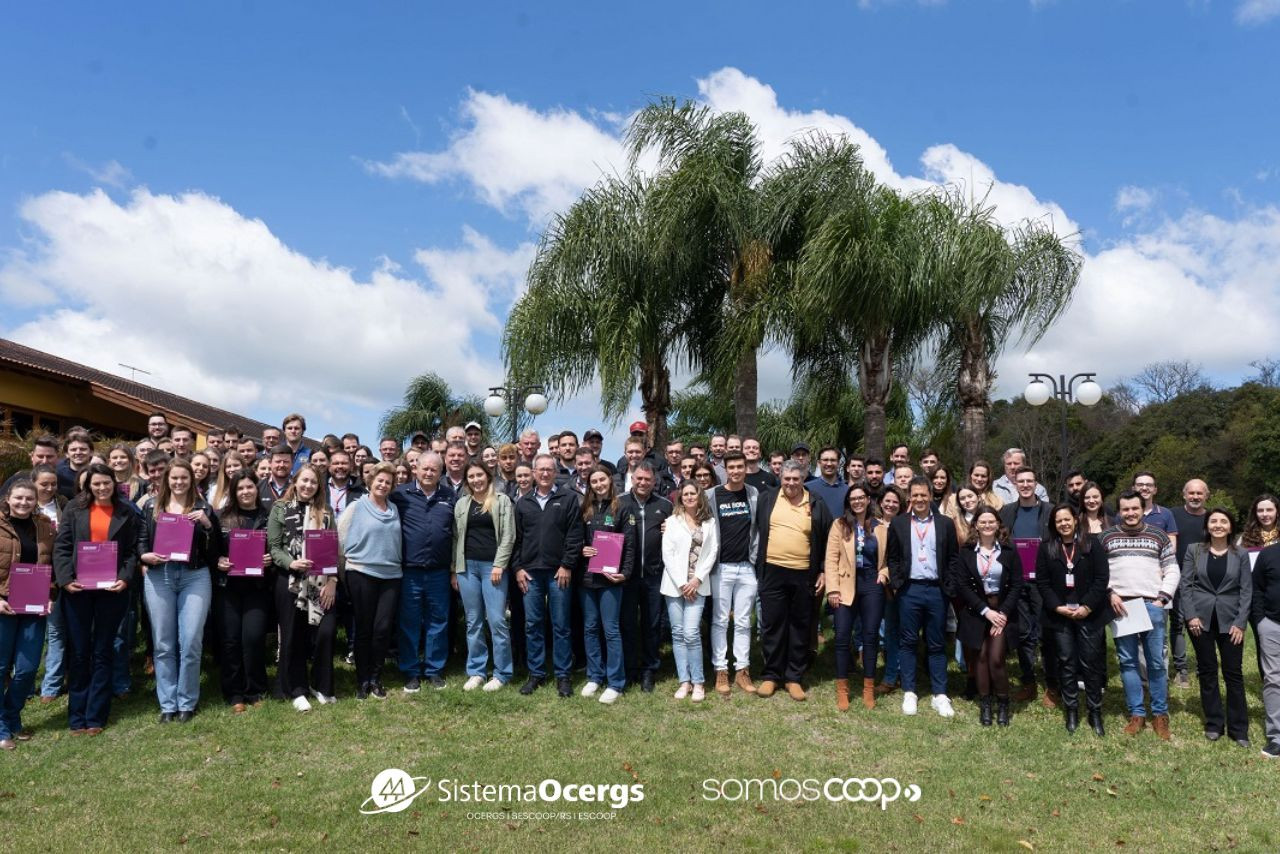 Jovens participantes do Programa Supernova da Cotrijal posam para foto em grupo durante encontro promovido pelo Sistema Ocergs e Escoop, em ambiente ao ar livre com palmeiras ao fundo.