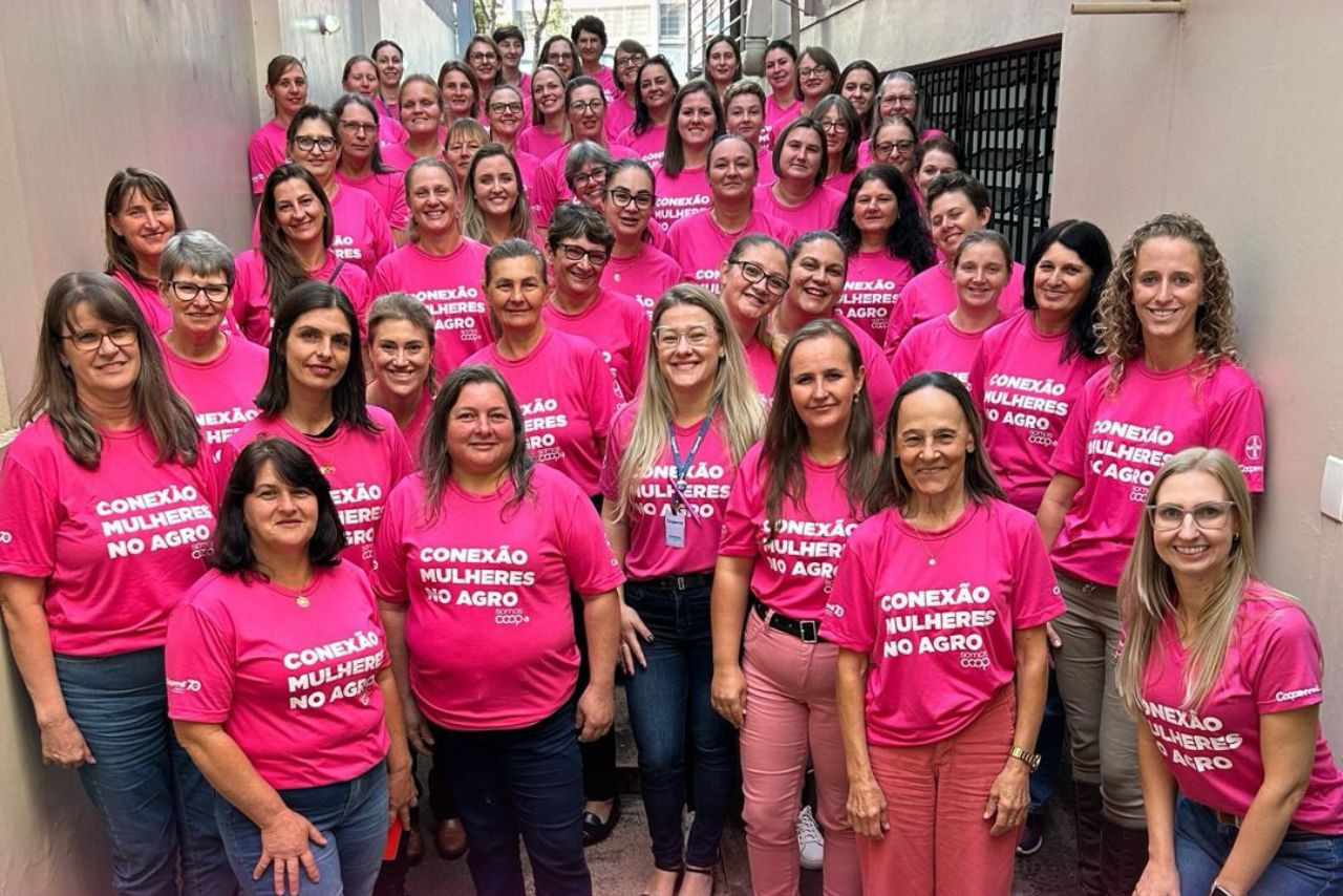 Grupo de mulheres da Coopermil reunidas com camisetas rosa do projeto "Conexão Mulheres no Agro", destacando a força feminina no cooperativismo e no agronegócio.